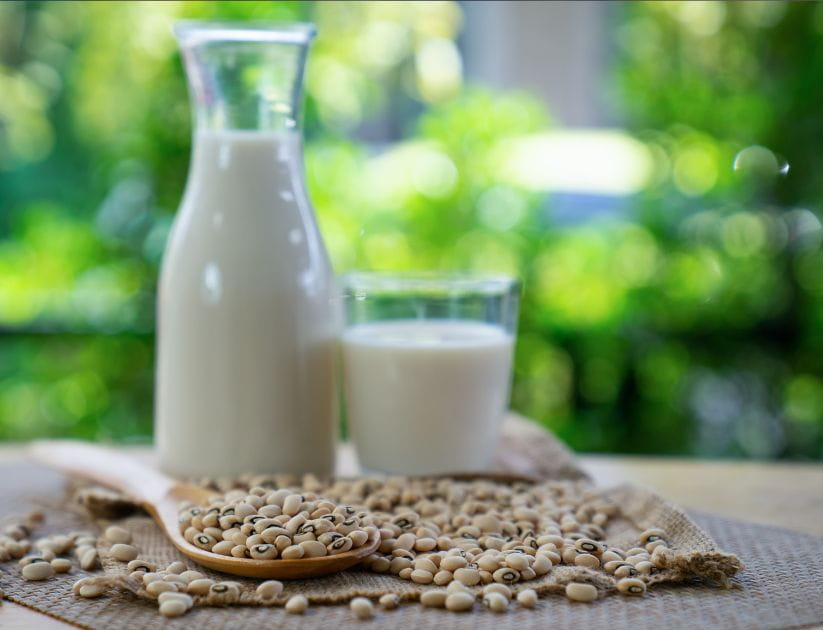 A glass of soy milk next to some soy beans on a wooden table
