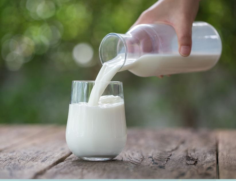 Whole milk being poured into a glass in front of a nature background