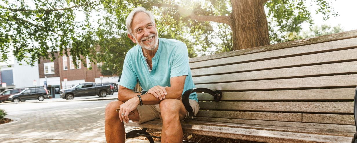  Happy retired senior man sitting on bench at park in city 