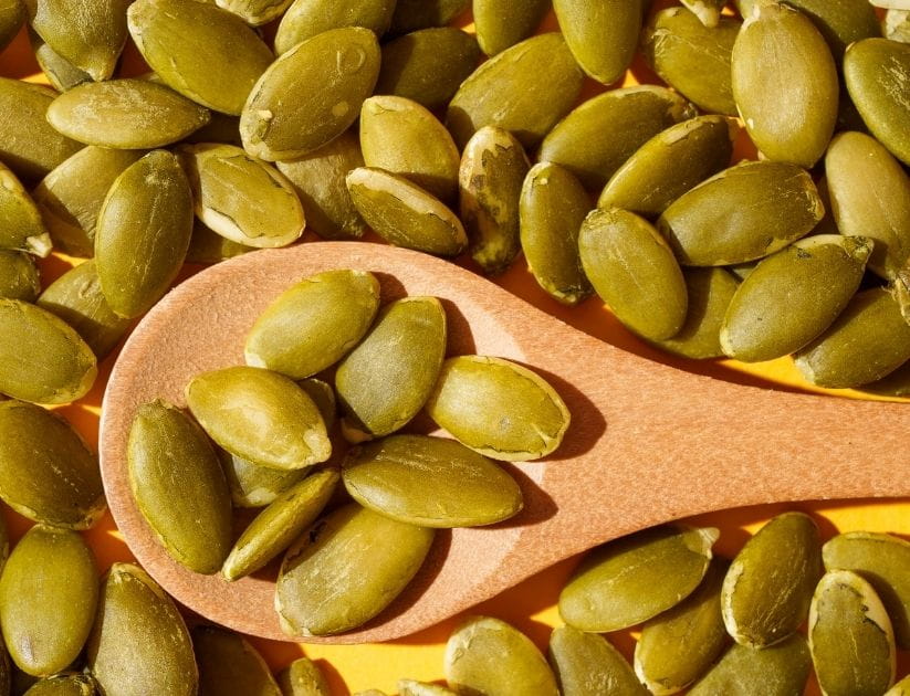 Pumpkin seeds scattered around a wooden spoon