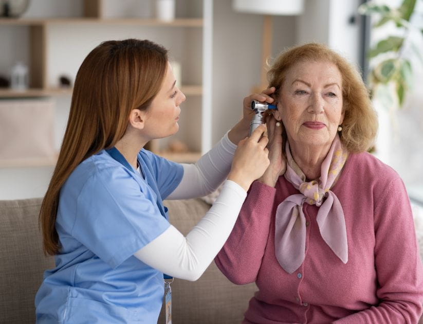 A caregiver gently examines a woman's ears with care as she smiles