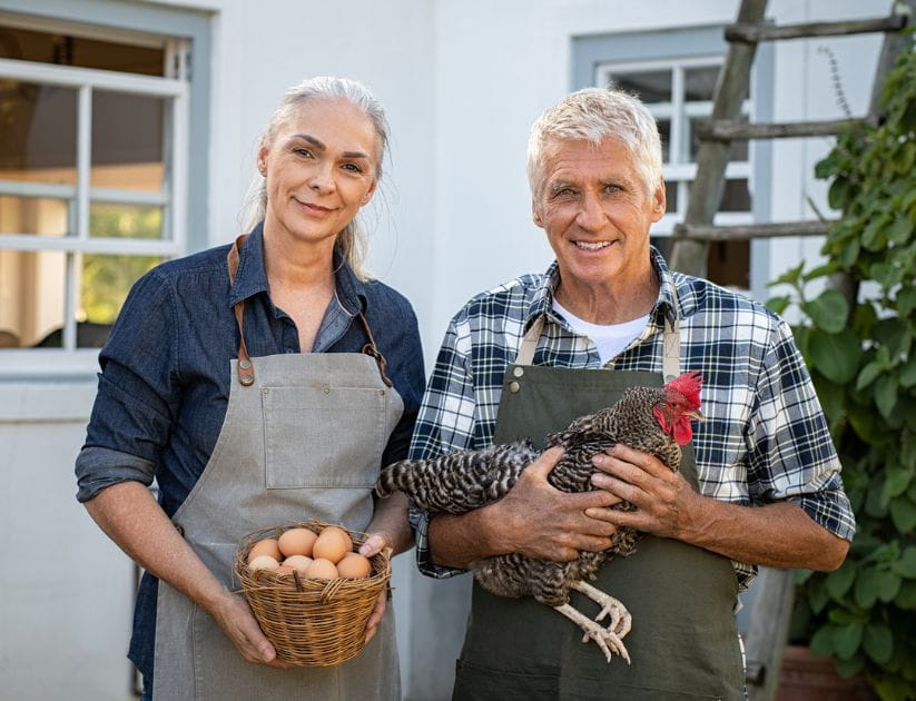 One person holding a chicken and the other holding a basket of eggs