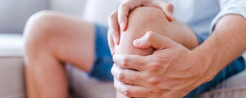 Close up of a mature man massaging his painful knee while sitting on a sofa