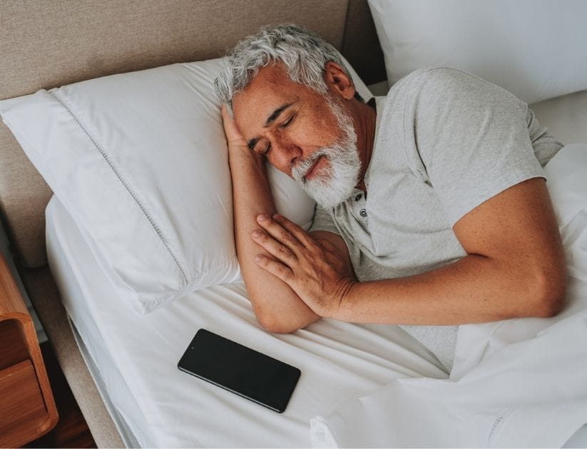  Portrait of an elderly man sleeping in bed with his cell phone beside him