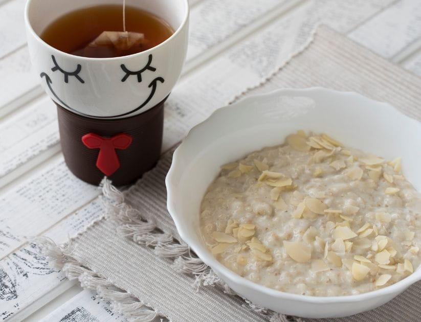 Bowl of porridge oats and some sliced almond and sunflower seeds. A healthy breakfast with a cup of team