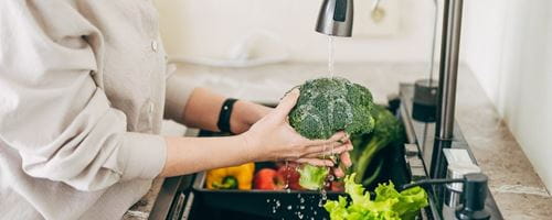 Hands of a person washing vegetables at the sink in the kitchen to prepare a fresh salad using tap water.