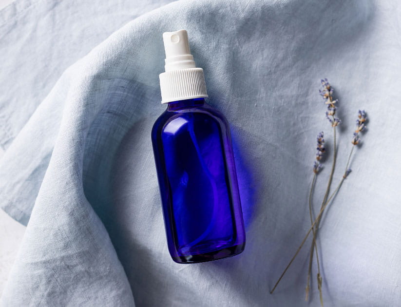 Top view of lavender spray in blue glass bottle on linen towel