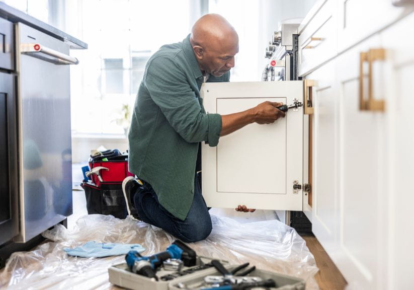 A man is knelt down changing the kitchen cupboard doors