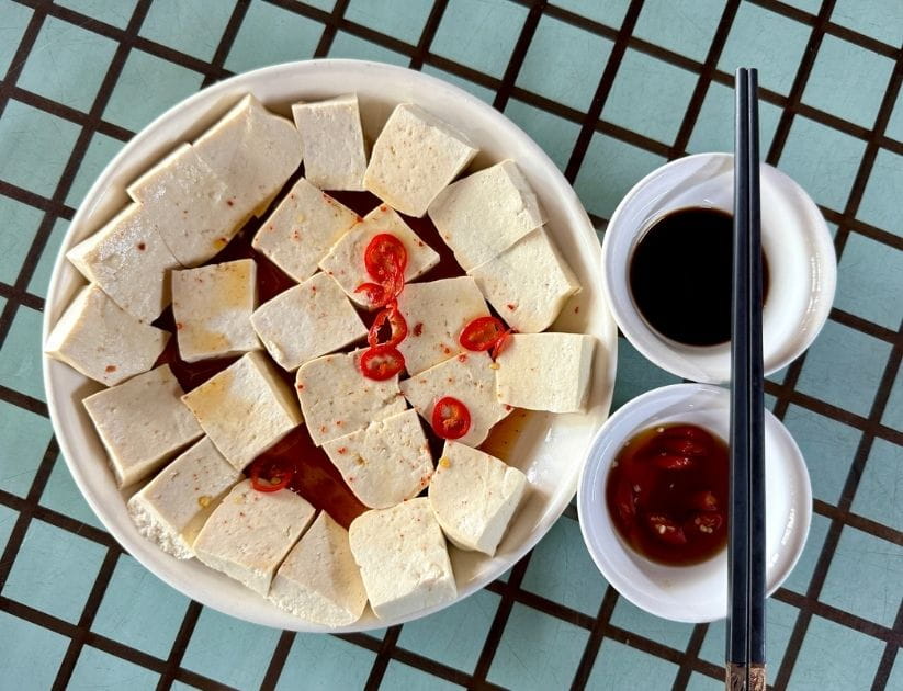  A plate of tofu with a sauce and garnished with chili slices.