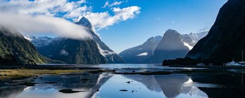 Cloudy mountain peaks reflect on water on a sunny day