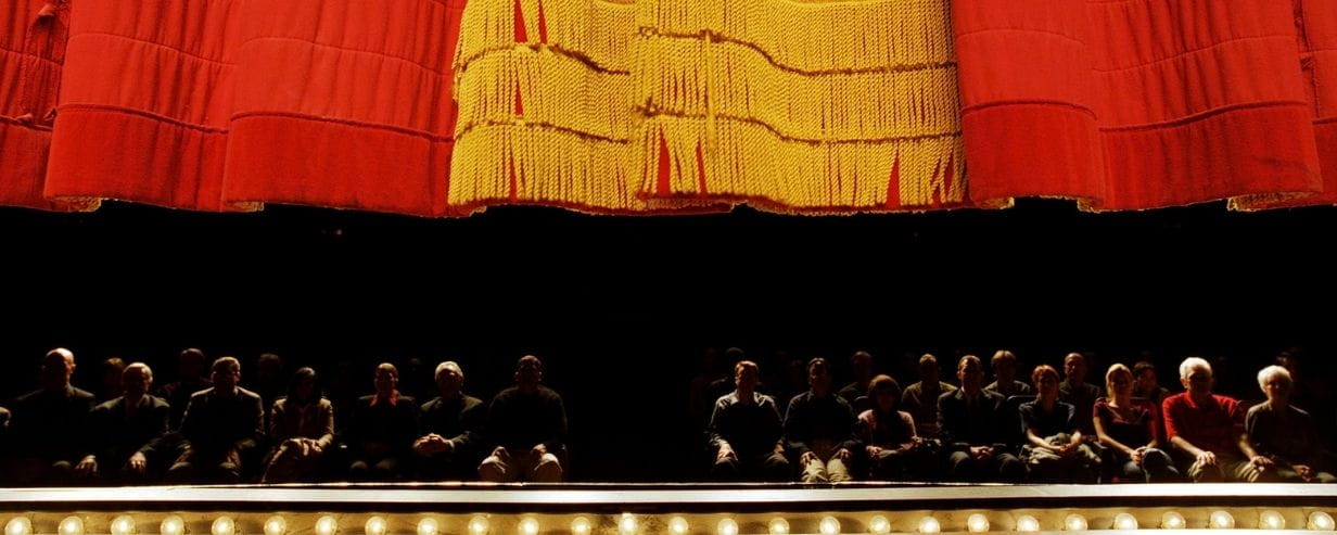 Red curtain descending on stage with the audience in background