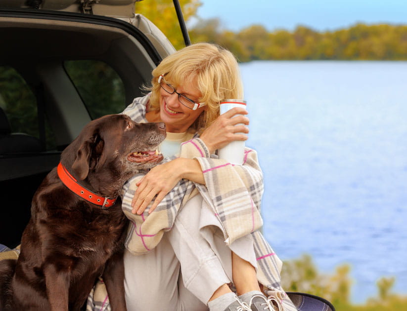 Mature woman enjoying time with her senior pet Labrador Retriever, while sitting in an open car boot