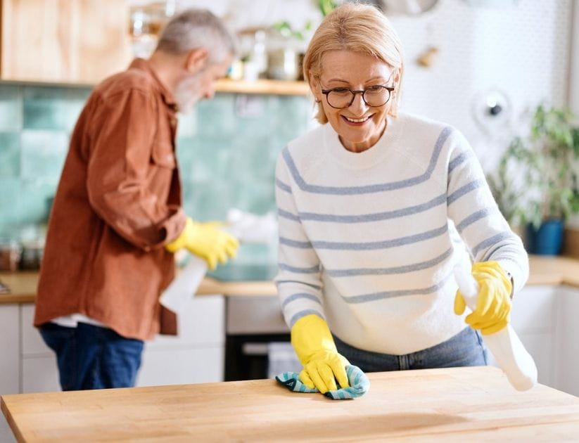  Woman is wiping the kitchen countertop, holding a cloth in one hand and a spray bottle in the other