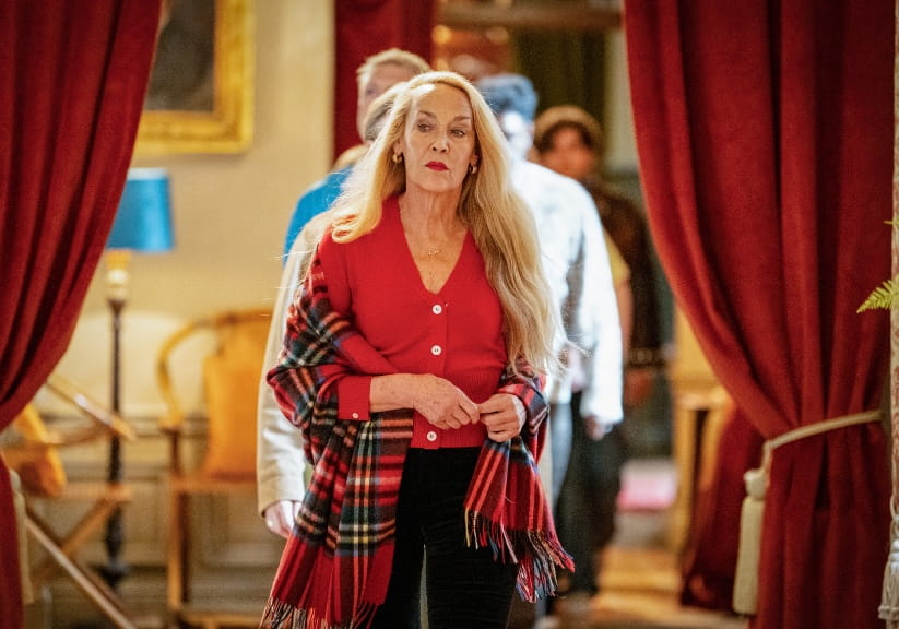 Jerry Hall walking between long red currtains in the Traitors castle