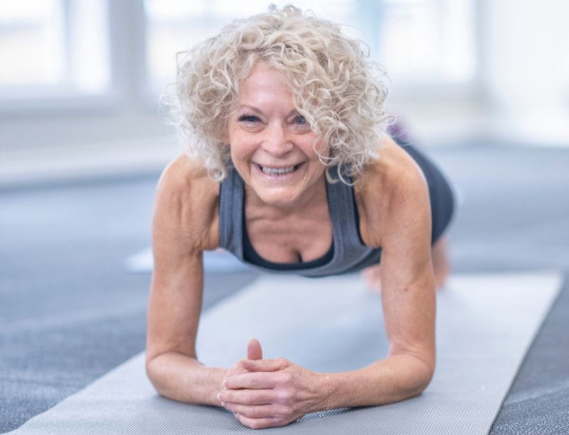 Image of a woman planking  on a yoga mat whilst smiling