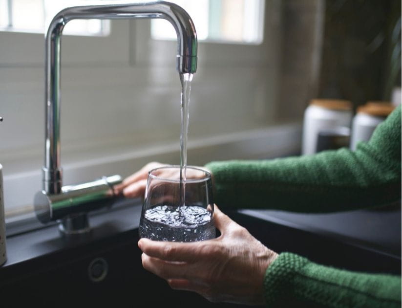Close up of a mature woman's hand filling a glass of filtered water right from the tap in the kitchen sink at home