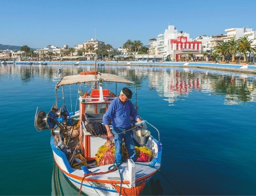 A man fishes on a boat in a harbour in Crete, Greece