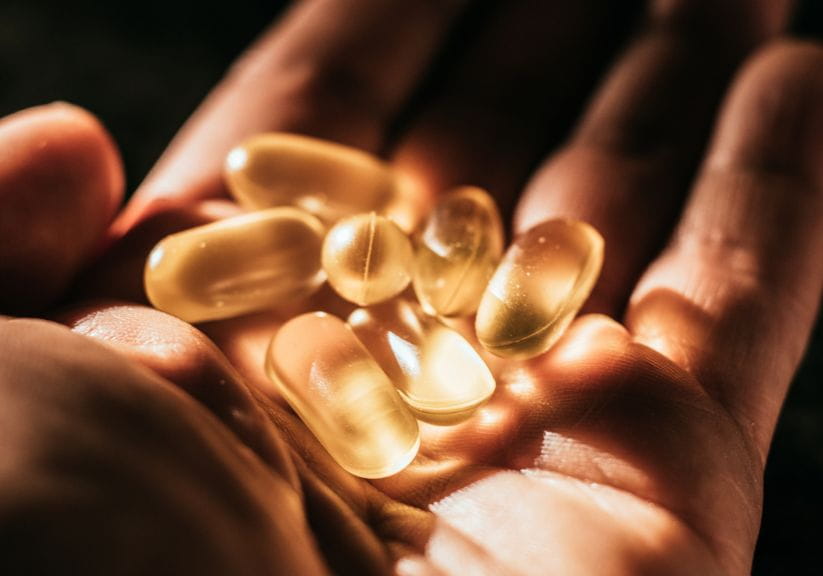 A person holding several vitamin D capsules in their hand in the sun