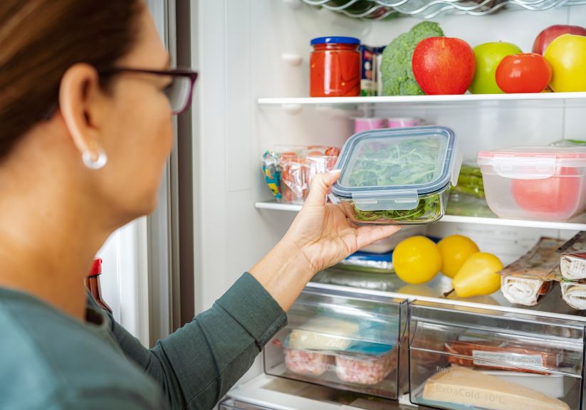 A woman looks at the food in her open fridge