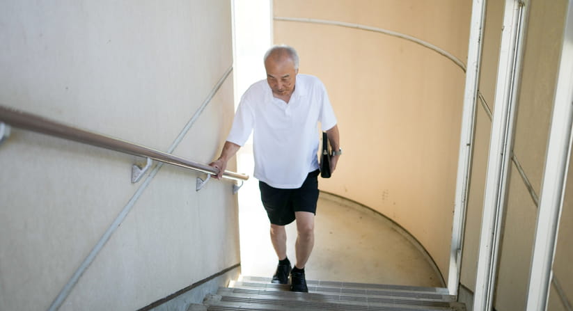 An older man in a white shirt and black shorts climbs a staircase