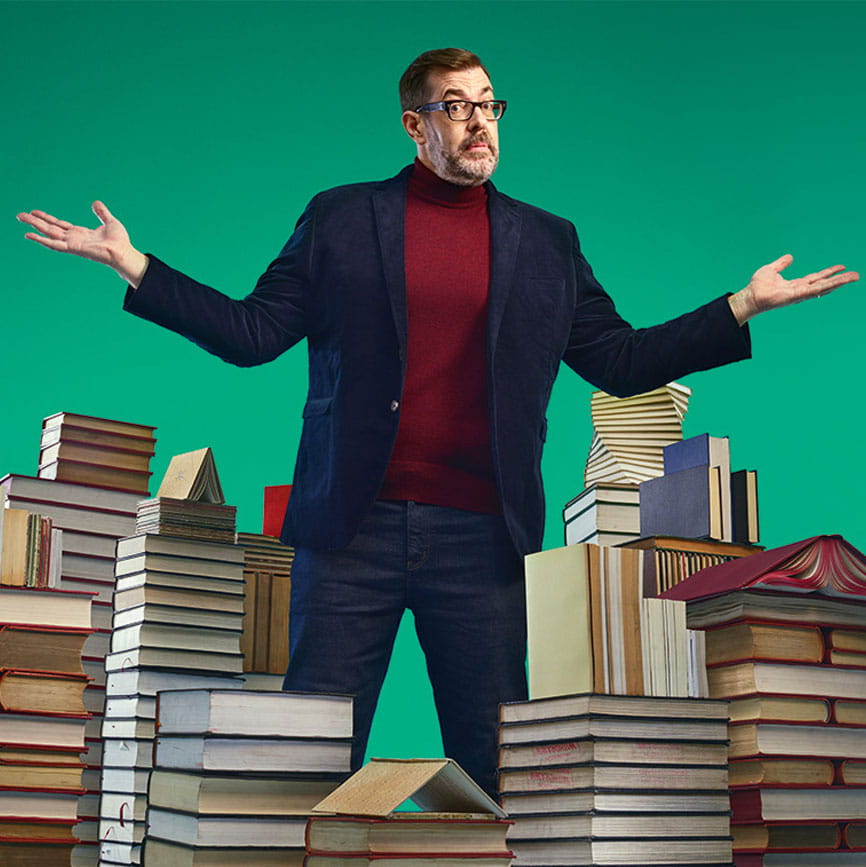 Richard Osman surrounded by piles of books
