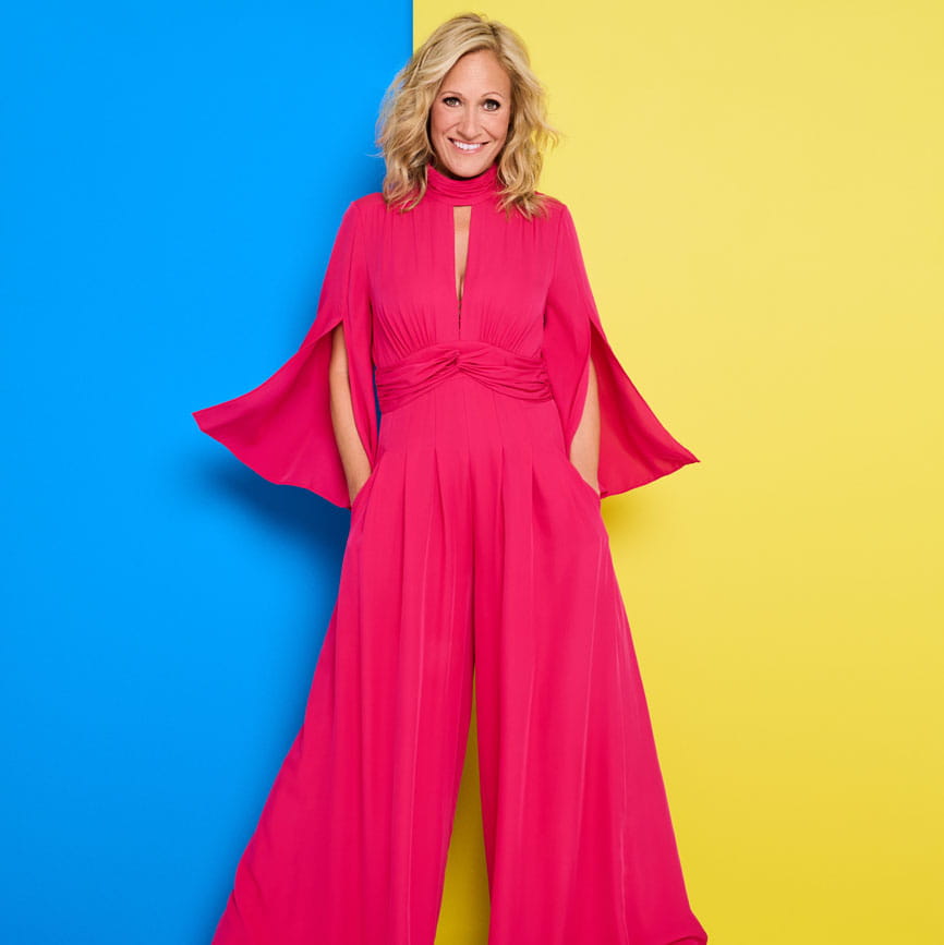 Sophie Raworth in a bright pink outfit on a blue and yellow background