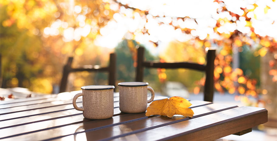 A pair of mugs on a garden table next to an autumnal leaf