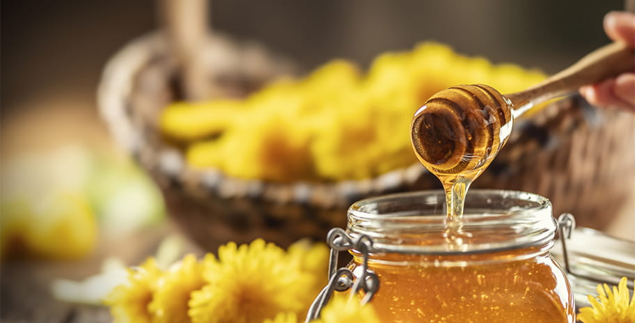 Honey in a jar in front of a basket of flowers