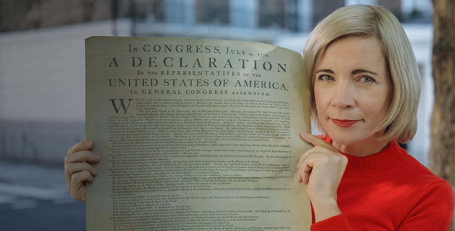 Lucy Worsley in a red jumper holding up the American Declaration of Independence