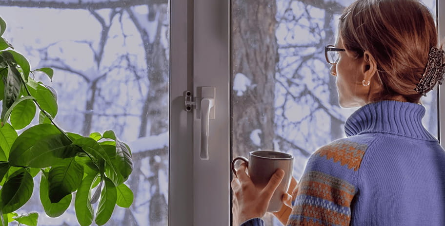 A woman holding a warm mug looking out the window