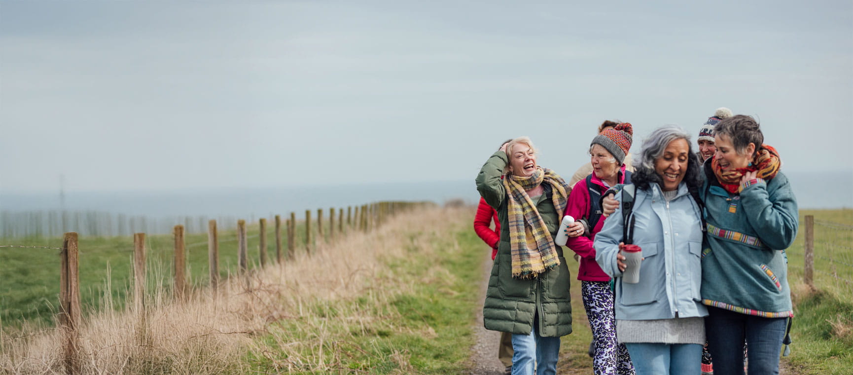 Four people dressed in warm clothing walking along a seaside path