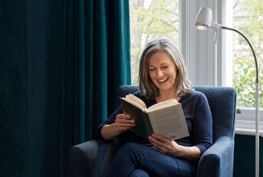 Mature woman in comfy chair reading a book with a Serious Readers light illuminating the pages