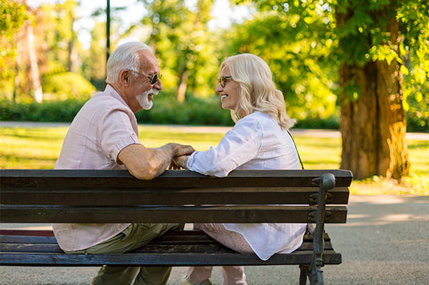 Senior adults smiling and chatting on a park bench surrounded by lush greenery