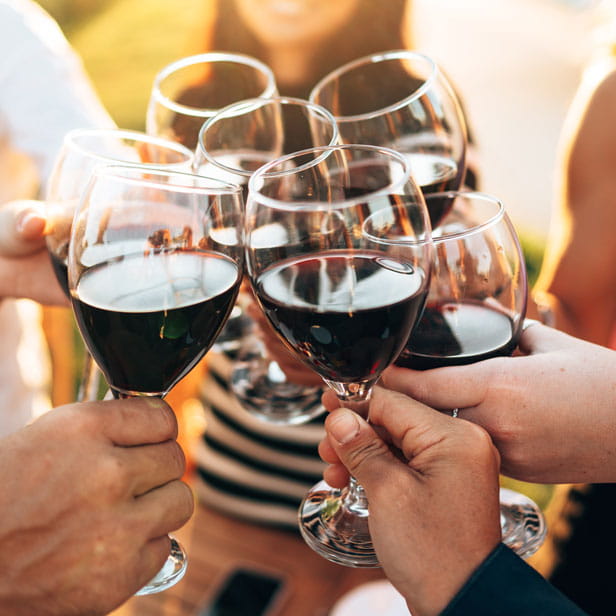 Four sets of hands holding glasses of red wine together in a cheers