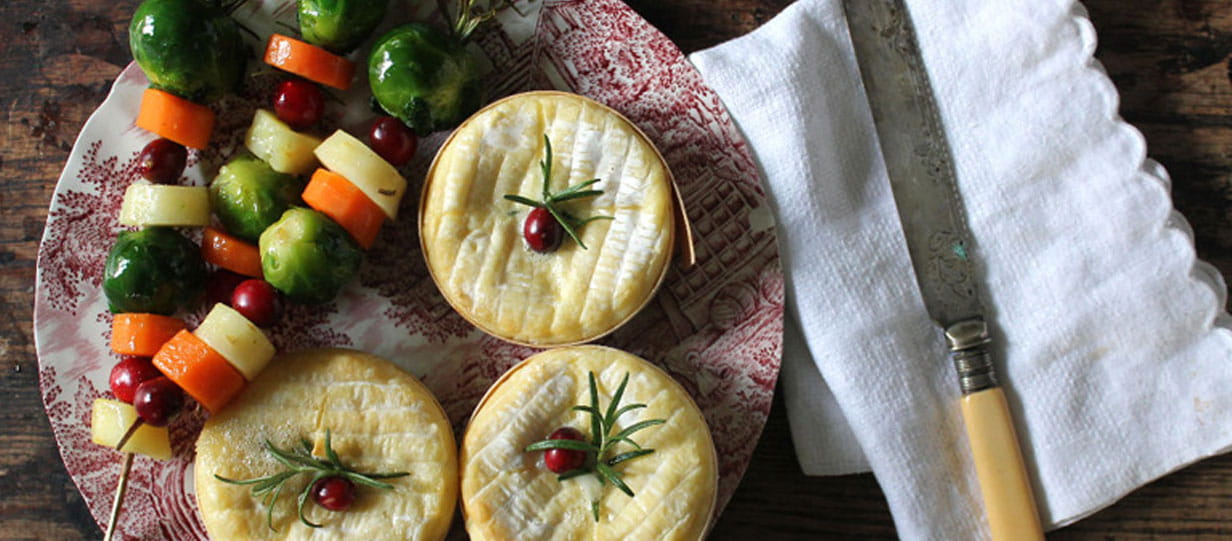 Three baked Camembert cheeses next to three vegetable skewers on a plate