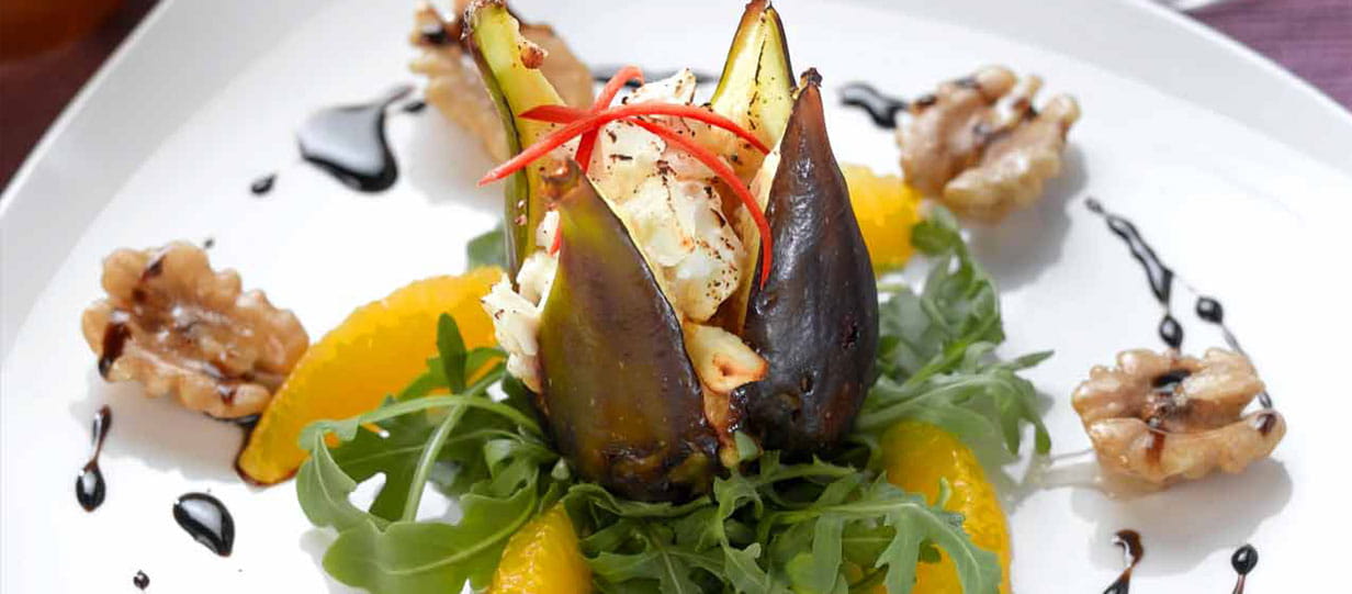 Fig on a plate garnished with rocket, walnuts and orange pieces