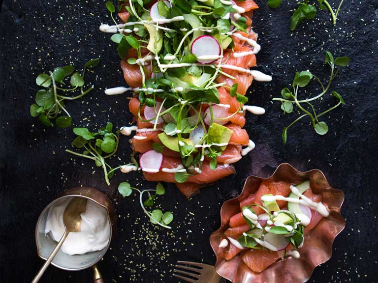 A plate of smoked salmon, dressed with watercress and radishes, on a black worktop