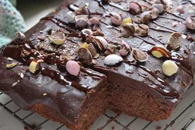 An Easter egg brownie cake, topped with mini Easter eggs, on a cooling rack with one square removed