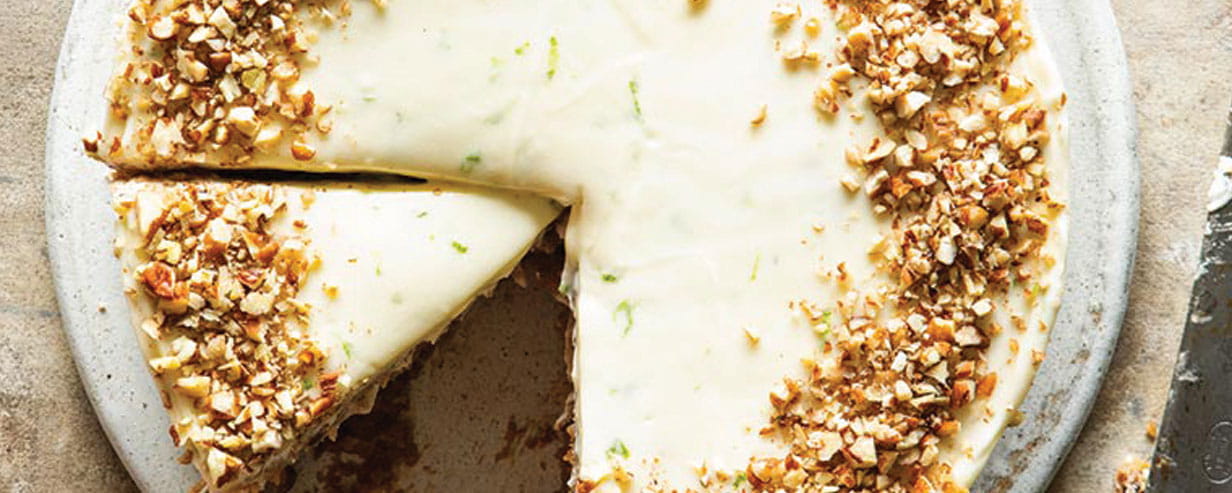 Top down view of a cake with white icing edged with a ring of chopped nuts and one slice removed