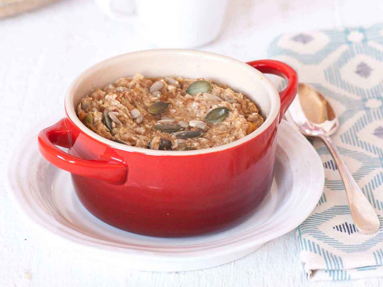 A small red pot filled with baked oatmeal and topped with pumpkin seeds