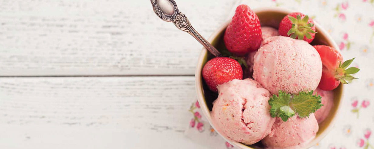 Scoops of strawberry ice cream in a bowl with fresh strawberries