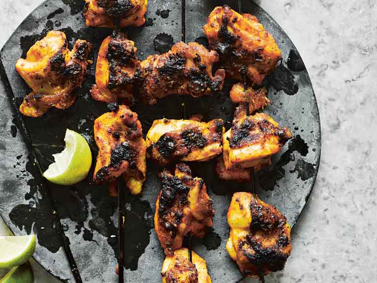 Grilled cubes of chicken on a black plate with a lime slice