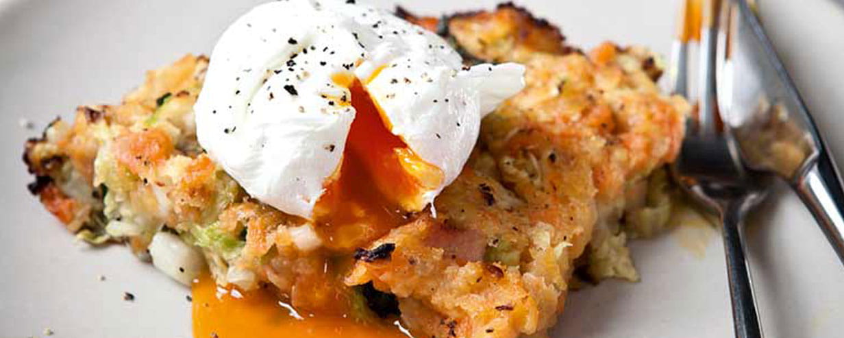 An opened egg with the egg running over a portion of bubble and squeak