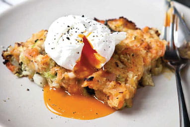 An opened egg with the egg running over a portion of bubble and squeak