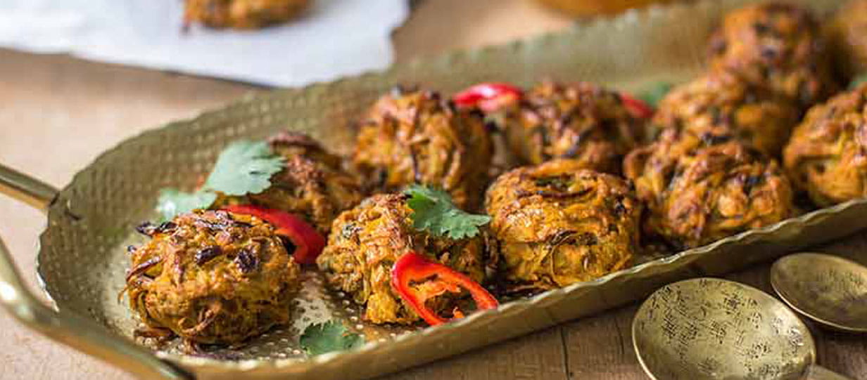 Potato and onion bhajis on a metal serving dish garnished with chilli slices and coriander