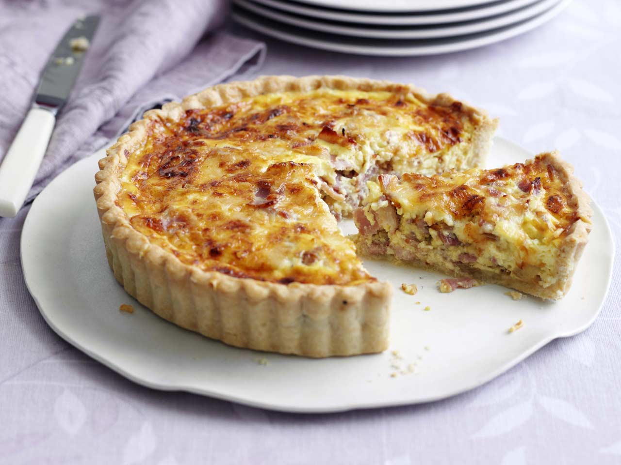 A quiche with bacon bits with a slice separated from the main part