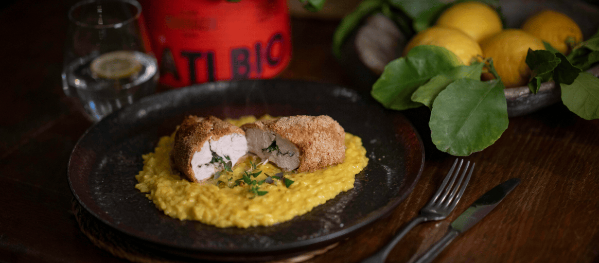 A plate of chicken Kiev with risotto on a wooden table