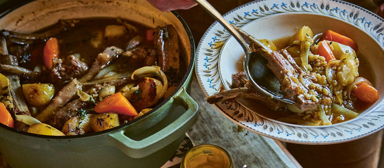 Clodagh McKenna's mum's irish stew with pearl barley in a cast iron pot with someone dishing a portion into a bowl next to it
