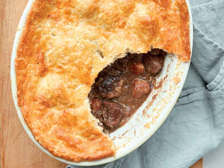 Mary Berry game pie in an oval pie dish - cut open to reveal meat and gravy filling