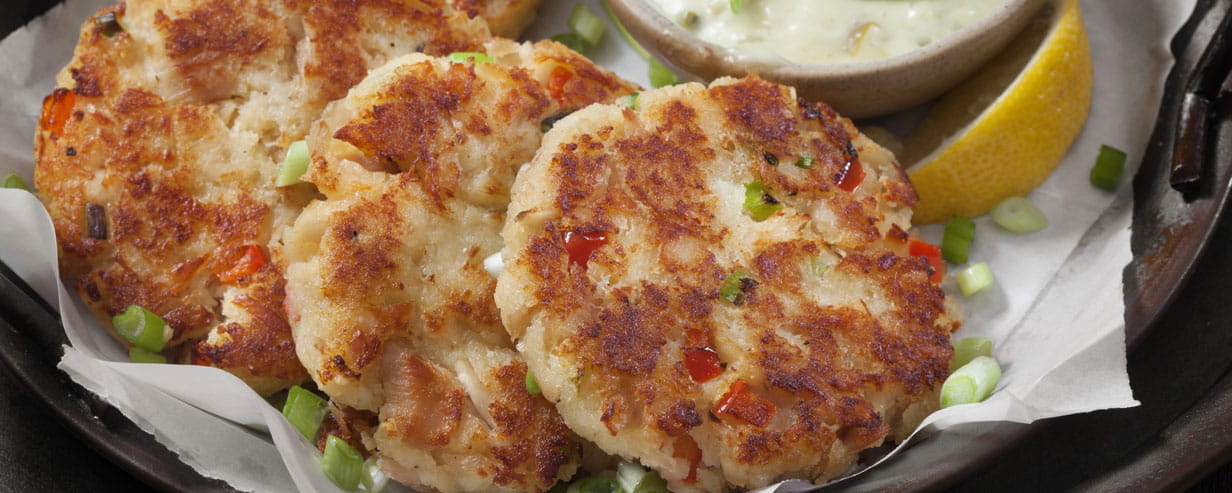 Four golden fishcakes on a plate garnished with chopped spring onion